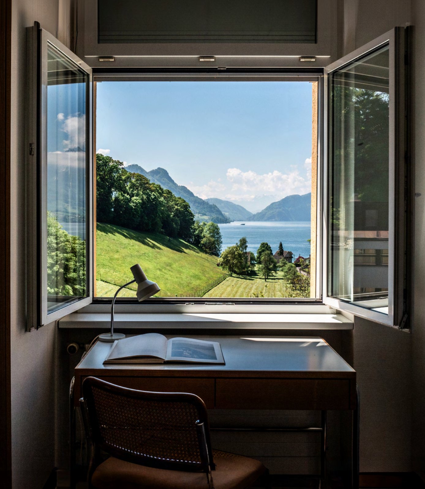 A desk by an open window overlooking Lake Lucerne